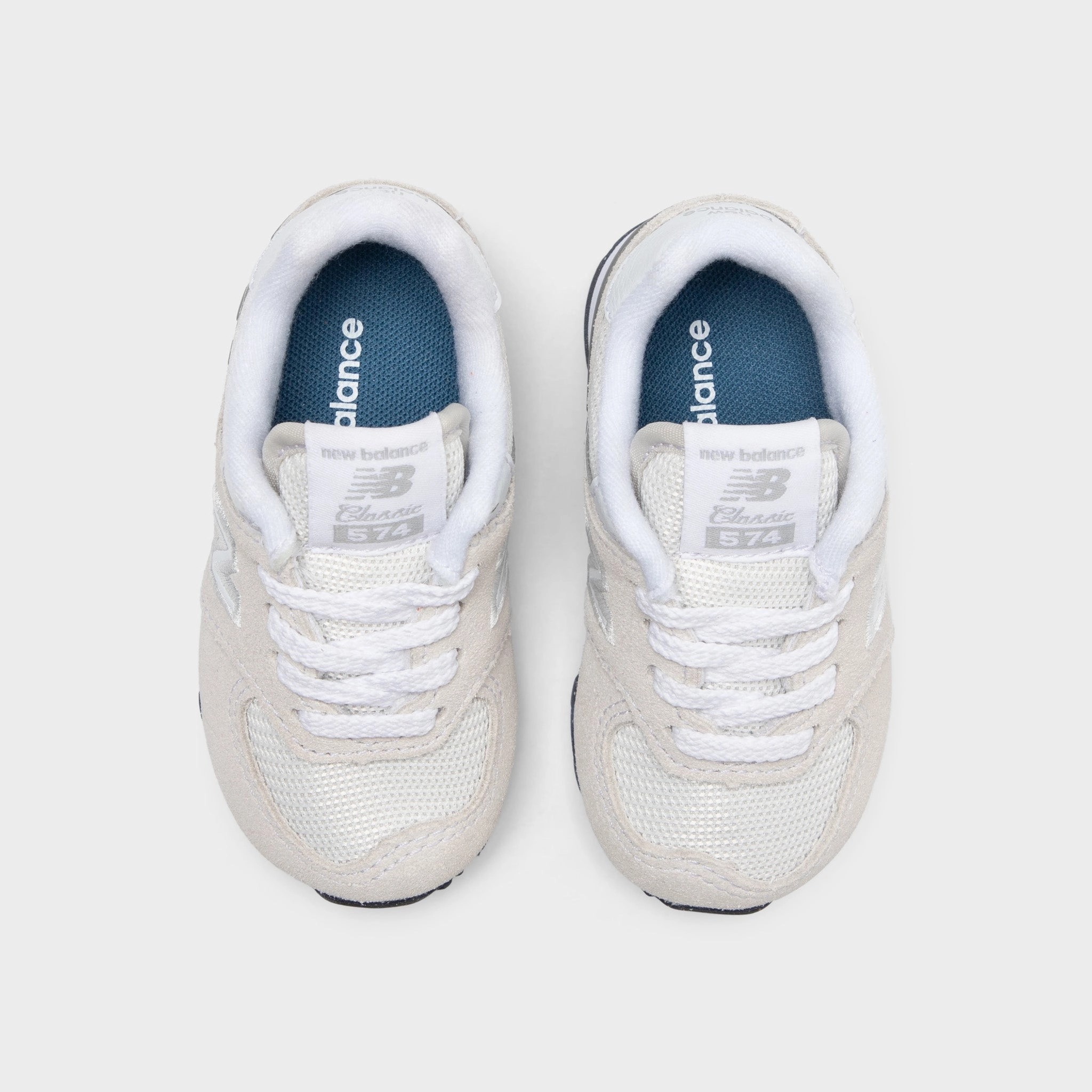 New Balance Infants' 574 Light Grey / White running on a dirt path Stable Heel